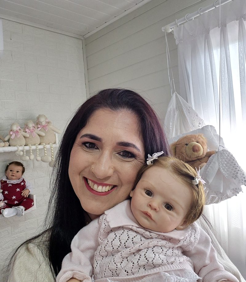 Artista da MiArts Reborn no ateliê, sorrindo ao lado de um bebê reborn
