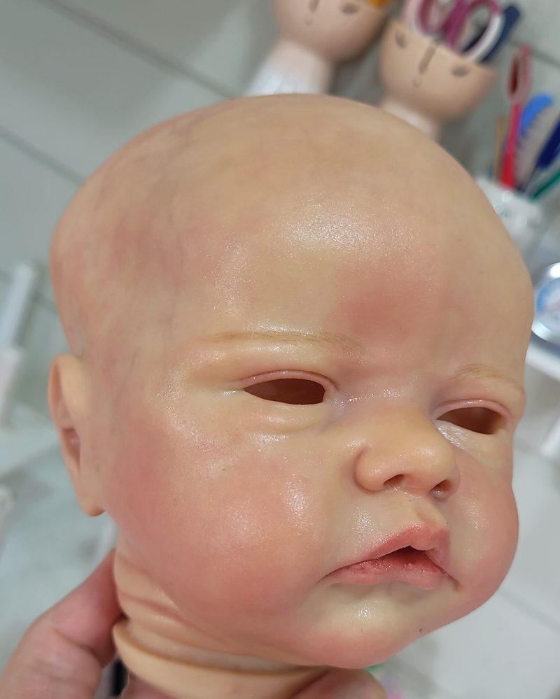 Detalhe da pintura em processo em um rosto de bebê reborn, ainda sem olhos