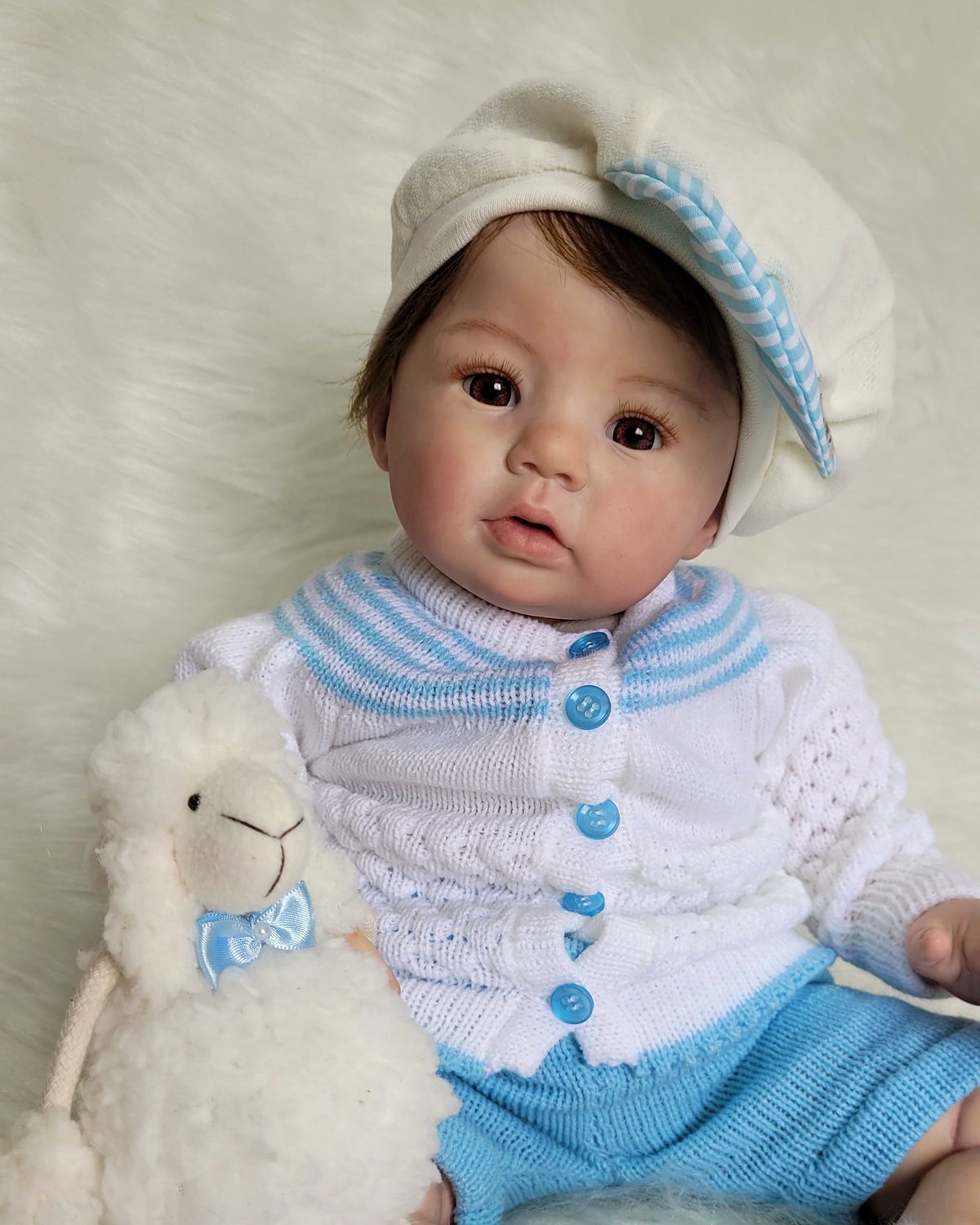 Bebê reborn menino com conjunto de tricô azul e branco, boina e ovelhinha de pelúcia