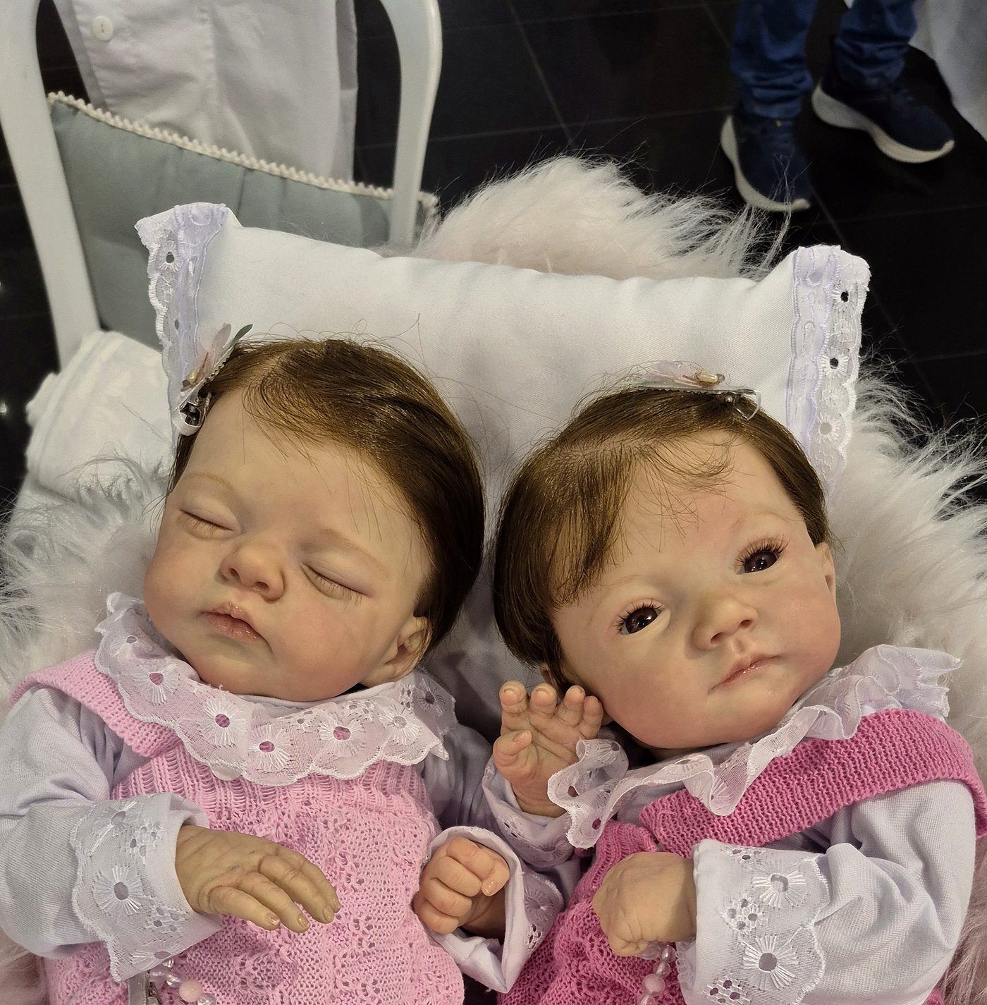 Duas bebês reborn lado a lado, com conjuntos de tricô rosa, renda e laços no cabelo