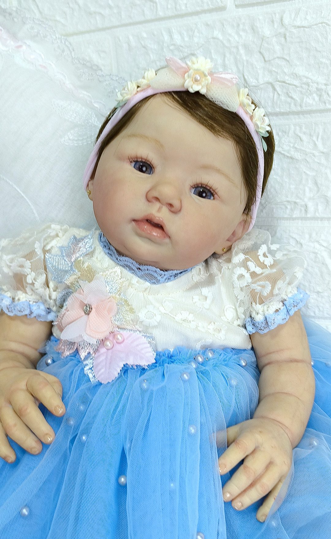Bebê reborn com vestido de tule azul, faixa de flores e olhar atento